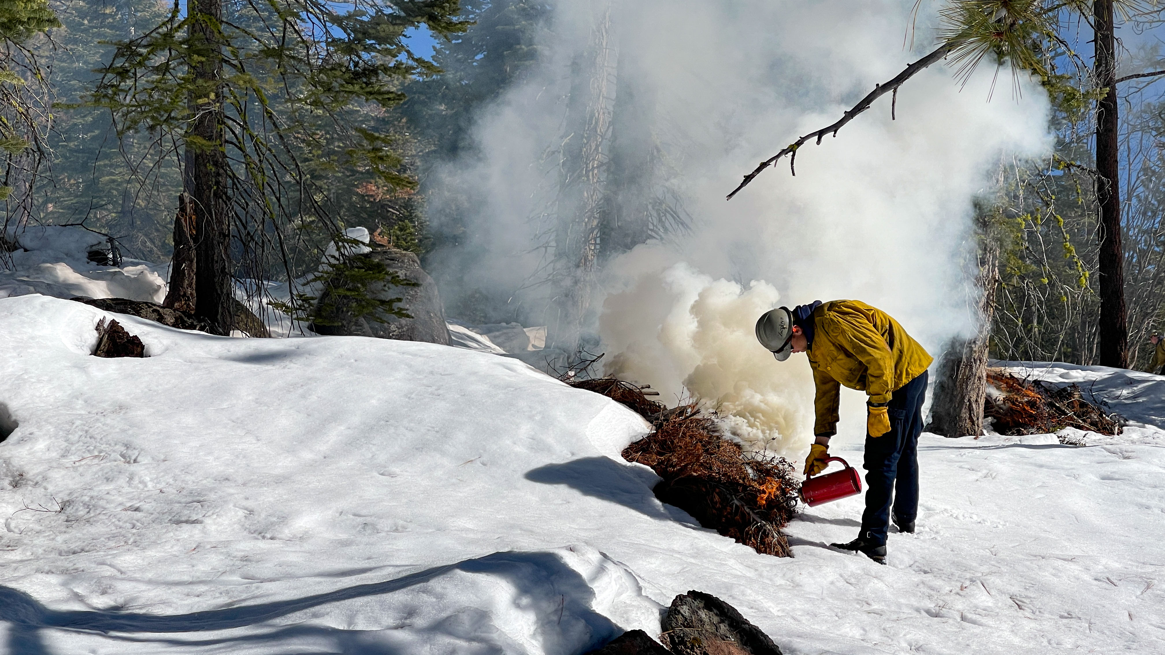 winter scene of a firefighter lights a pile using a drip torch