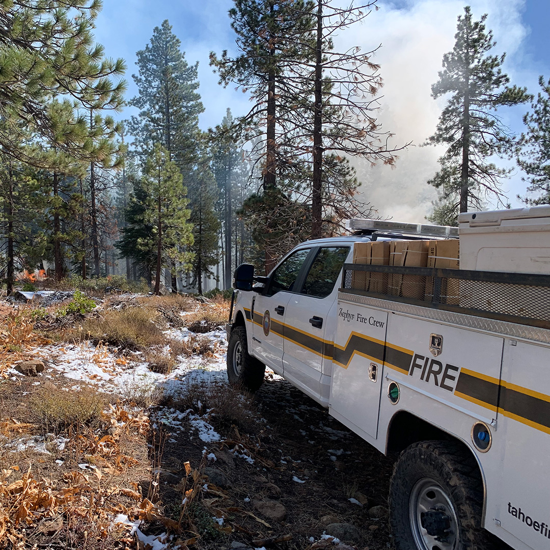 A Tahoe Douglas Fire Protection District truck and forest with prescribed fire operations in the background.