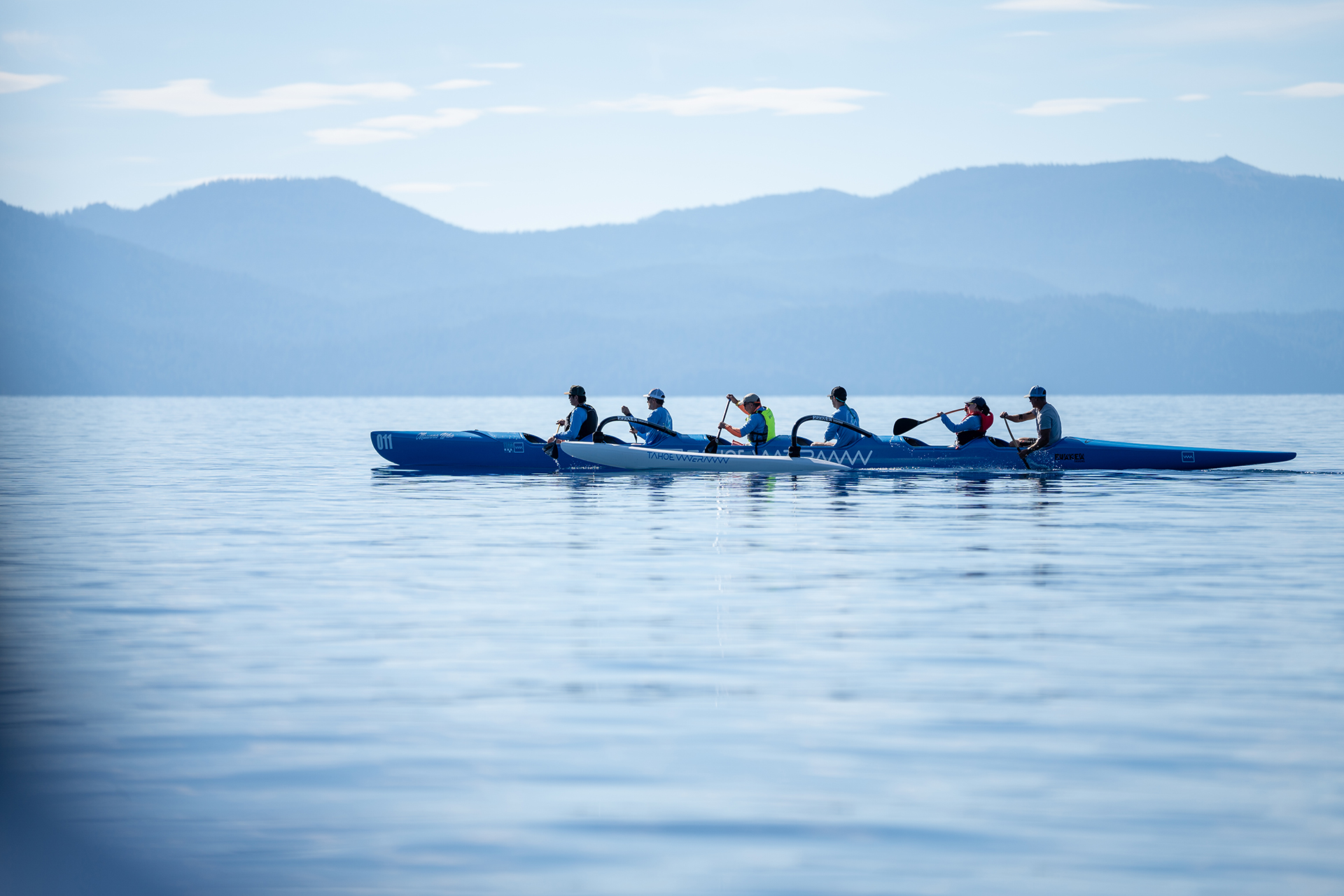 People paddling an outrigger canoe on Lake Tahoe with mountains behind